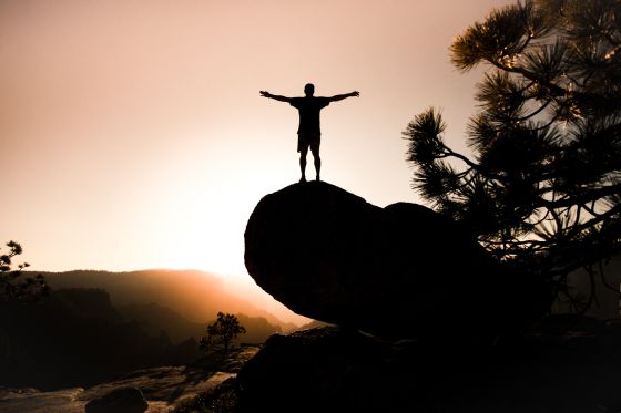 Man on rock in sunset with arms stretched out experiencing independence